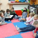 Dzieci siedzą na dywanie w świetlicy jedno dziecko czyta książkę na głos