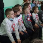Dzieci na widowni z kotylionami biało-czerwonymi oglądają akademię