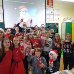 Dzieci ubrane na czerwono i w czapkach Mikołaja stoją pokazują swoje prezenty