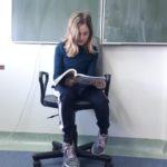 Uczennica siedząc przy tablicy na krześle czyta książkę