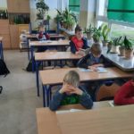 Uczniowie siedzą w ławkach w klasie i czytają książki