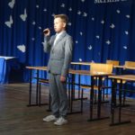 Uczeń ubrany odświętnie recytuje wiersz o nauczycielach na akademii z okazji Dnia Edukacji Narodowej