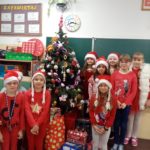 Dzieci stoją w czapkach Mikołaja przy choince