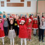 Dzieci ubrane na czerwono i w czapkach Mikołaja ćwiczą z podniesionymi rękami