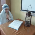 Scenki z Biblii dziewczynka przebrana za anioła klęczy i czyta Pismo święte