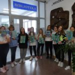 Jedenaście dziewcząt z książkami o sporcie przed wejściem do biblioteki szkolnej
