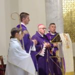 Biskup czyta w kosciele w otoczeniu księży i stojącego obok ministranta