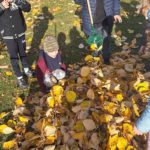 Dzieci stoją wokół gromadki zagrabionych liści