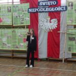 Narodowe Święto Niepodległości w SP 4 - uczennica na tle dekoracji recytuje wiersz patriotyczny