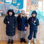 Dwie dziewczynki trzymają parasole, a inna dziewczynka ubrana jest w ciepłą czapkę i kurtkę