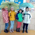 Dwie osobyi trzymają parasole, a inne dzieci ubrane są w ciepłe czapki i kurtki