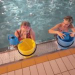 Andrzejki na Pływalni Miejskiej - dwie dziewczynki wlewają wodę z konewek do wiader