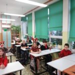 Mikołajki w SP 4 - dzieci ubrane na czerwono i w czapkach Mikołaja siedzą w ławkach
