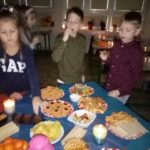 Troje dzieci stoi przy stole z ciastkami i owocami
