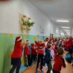Ubrane na czerwono dzieci i w czapkach mikołajowych tańczą na korytarzu