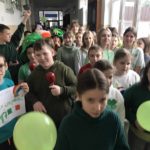 Korowód uczniów ubranych na zielono idący korytarzem szkolnym